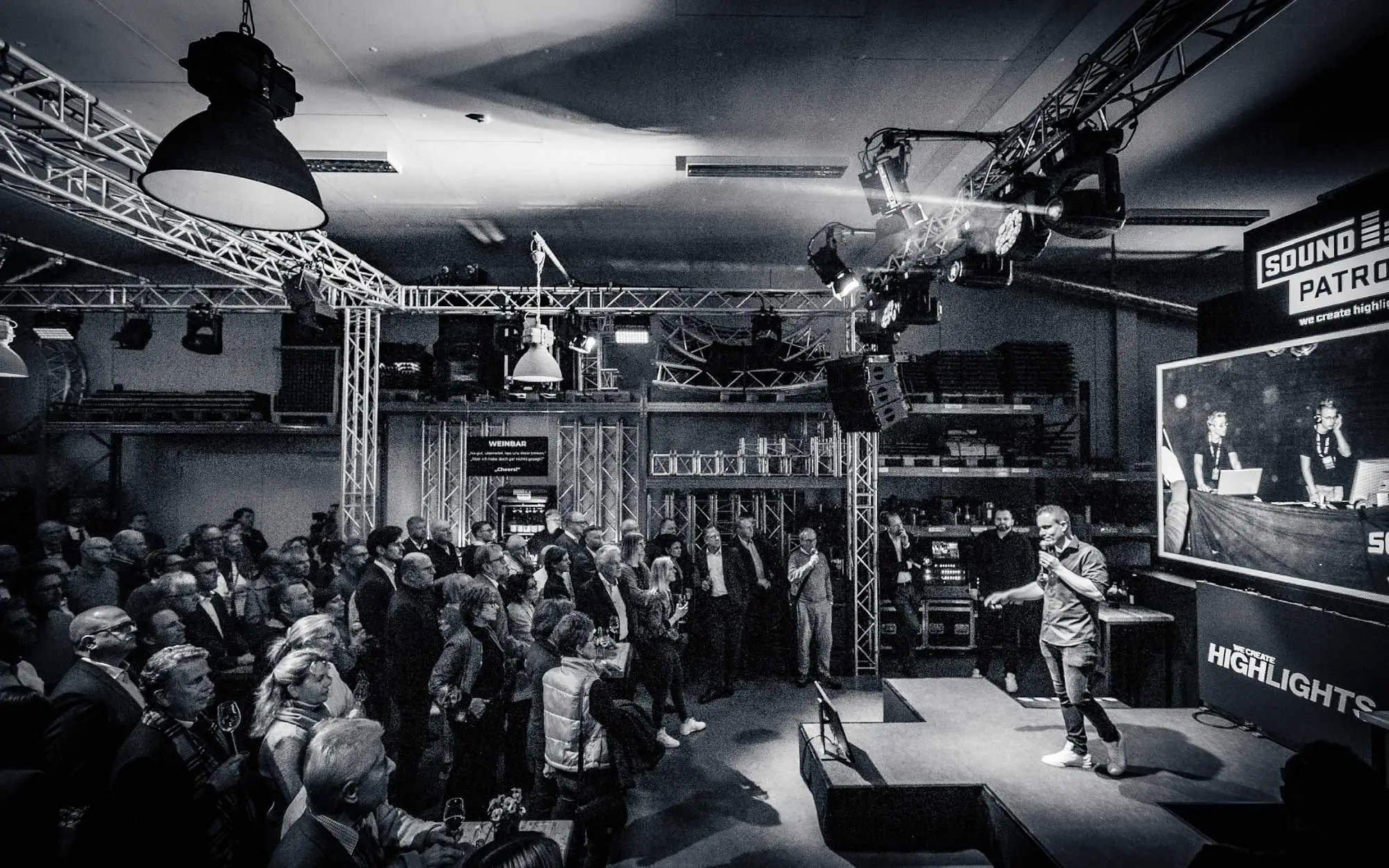 K-Treff Rotenburger Wirtschaftsforum bei Sound Patrol: Referent auf der Bühne in der Sound Patrol Lagerhalle, schwarz-weiß Fotografie