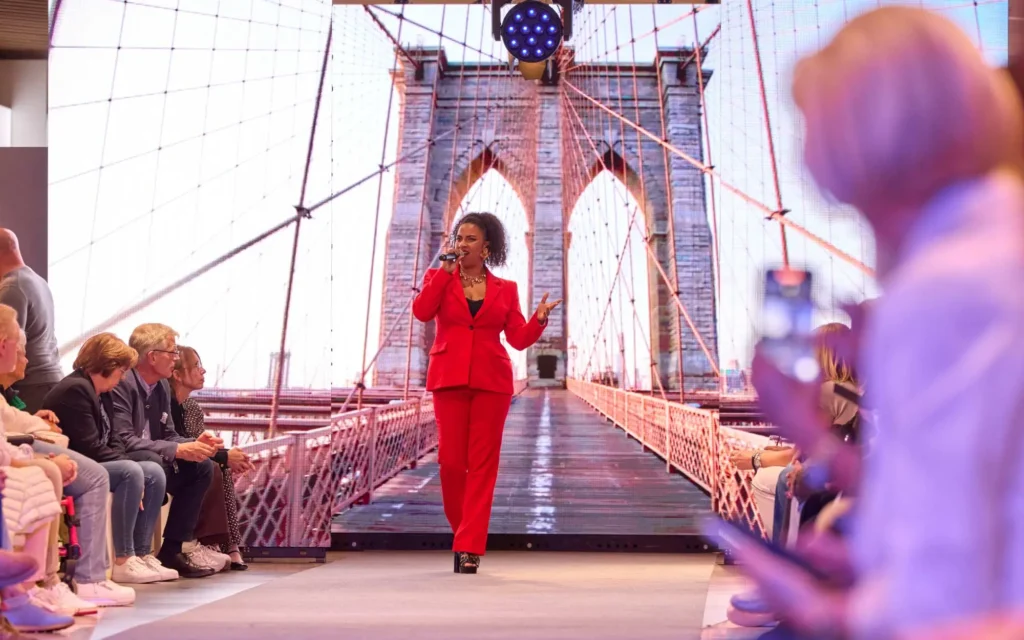 Sound Patrol Dodenhof VIP Fashion Night: Sängerin im roten Anzug auf dem Laufsteg vor großer LED-Wand mit Brooklyn-Bridge-Motiv