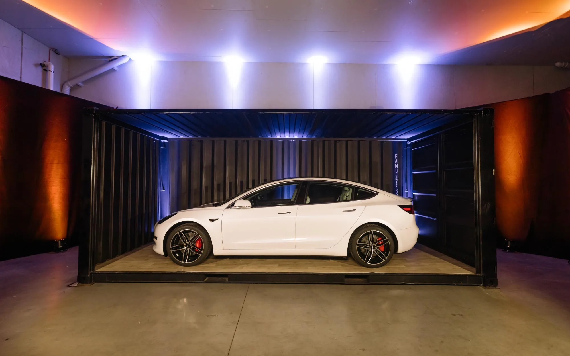 Sound Patrol Produktpräsentation: Weißer Tesla in modernem Container-Showroom mit professioneller Lichttechnik